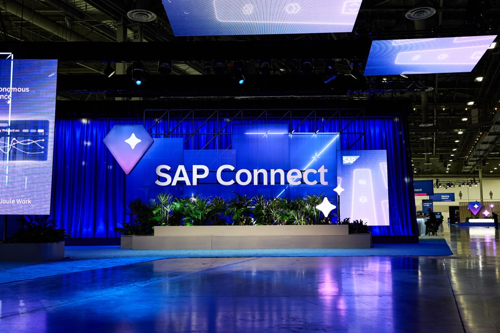Escenario decorado para el evento SAP Connect con cortinas azules y plantas en el frente, mostrando el logotipo de SAP.